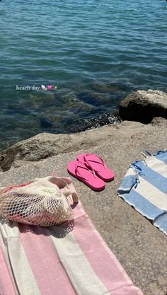 two pairs of pink flip flops sitting on top of a towel next to the ocean