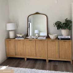 a wooden dresser with a mirror on top of it next to a lamp and potted plant