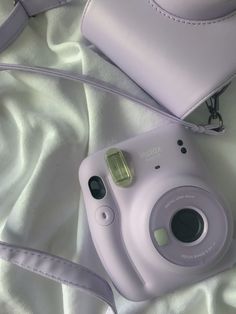 a white camera sitting on top of a bed next to a purple purse and strap