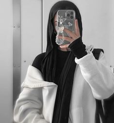 a woman wearing a hoodie taking a selfie with her cell phone in the mirror