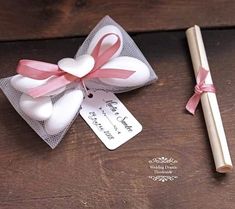 a pen and some paper on a wooden table next to a small gift bag with a pink ribbon