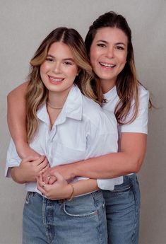 two young women hugging each other in front of a gray background