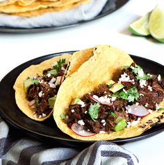 two tacos with meat, onions and cilantro are on a black plate