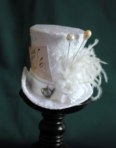 A Mad Hatter mini top hat with a bridal twist! The hat is covered with beautiful textured white brocade and embellished with white taffeta ribbon around the crown. Trimmed with pearl hats pins, white roses,white feather spray, the signature 10/6 Mad Hatter card and of course a tiny silver tea-pot! Cause around here it's always tea-time! Both hat pins have push-in clasps to avoid accidents! IMPORTANT NOTE: The fabric used in the original design is permanently OUT OF STOCK. Please check out the NE Fitted Brimmed Top Hat For Themed Events, Vintage Top Hat With Short Brim For Themed Events, Whimsical Fitted Top Hat With Short Brim, Vintage Mini Hats With High Crown For Themed Events, Vintage Brimmed Mini Hats For Themed Events, Vintage White Top Hat For Formal Occasions, White Vintage Top Hat For Formal Occasions, White Vintage Top Hat With Curved Brim, White Fitted Vintage Top Hat