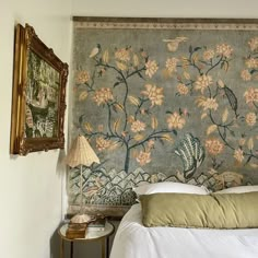 a bed sitting in a bedroom next to a wall with flowers on it and two framed pictures