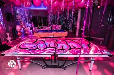 a table with pink and purple decorations in the middle of a room filled with balloons