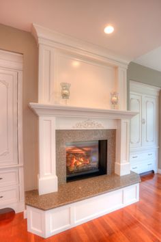 a fireplace in the middle of a room with white cupboards and wood flooring