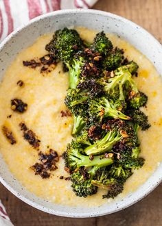 a bowl filled with broccoli and cheese on top of a wooden table next to a napkin