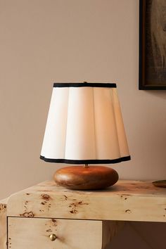 a lamp sitting on top of a wooden table next to a painting and an old dresser