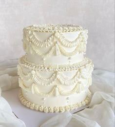 a three tiered white wedding cake with pearls on the top and sides, sitting on a table cloth