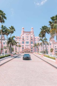 a car parked in front of a large pink building with palm trees on both sides