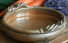 a brown bowl sitting on top of a wooden table next to carrots and broccoli