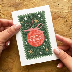 two hands holding up a christmas card on top of a wooden table