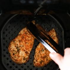 someone is using tongs to fry some food in an air fryer with two pieces of chicken on it