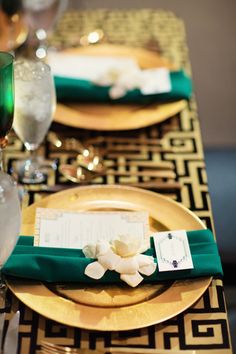 the place setting is set with gold plates and green napkins, which are accented with white flowers