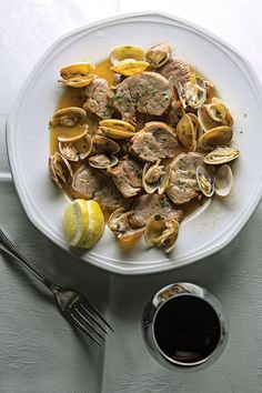 a white plate topped with clams and sliced lemons on top of a table