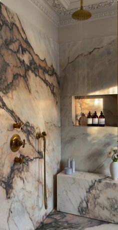 a bathroom with marble walls and flooring, gold faucets and shower head