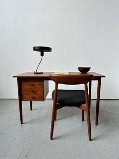 a desk with a lamp on it and a chair next to it in front of a white wall