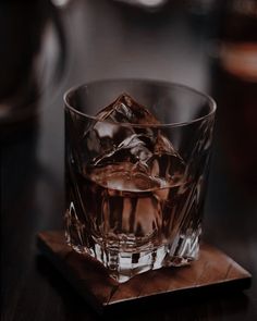 an old fashioned glass with ice cubes on a wooden coaster