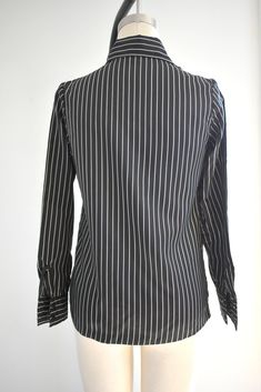 "Description: 1970s black and white striped silky polyester blouse. Long sleeves with pleated shoulders. Button front. Condition: In great condition, with no holes or stains. Designer: It's Gailord Stated Size: 10 Measurements: Armpit to armpit: 18\" Shoulder to shoulder: 14.5\" Sleeve length: 23\" Overall length: 23\" Waist: up to 35\" ---> If you need an order shipped by a particular date or shipped via a quicker method, please ask PRIOR to purchase to see if we can accommodate that request Elegant Pinstripe Button-up Blouse, Black Long Sleeve Blouse With Vertical Stripes, Classic Black Shirt With Vertical Stripes, Black Collared Blouse With Striped Collar, Striped Business Tops With Buttons, Black Long Sleeve Blouse With Striped Collar, Classic Formal Blouse With Striped Collar, Pinstripe Blouse With Button Closure For Work, Business-style Collared Top With Vertical Stripes