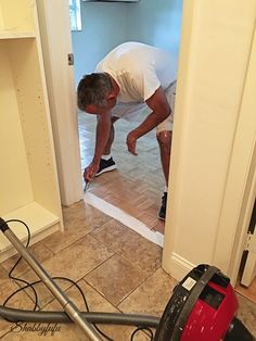 a man in white shirt using a vacuum to clean the floor with a red and black blow dryer