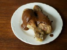 two pieces of chicken on a white plate covered in chocolate sauce, sitting on a wooden table