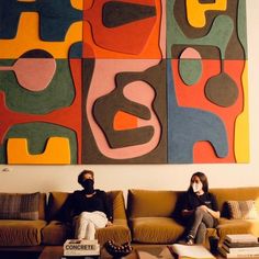 two people sitting on a couch in front of a large abstract painting over a coffee table