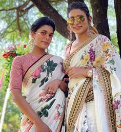 two women standing next to each other in front of a tree with flowers on it