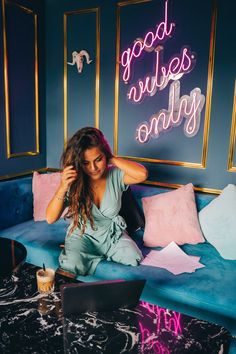 a woman sitting on top of a blue couch in front of a neon sign that reads good news only