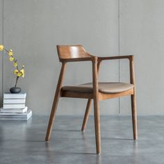 a wooden chair sitting next to a vase with flowers in it on a gray floor