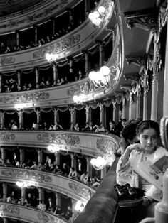 an old black and white photo of people sitting on the balcony of a theater with chandeliers