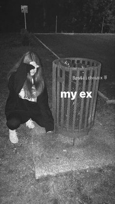 a woman sitting on the ground next to a trash can with her head in her hands