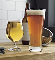 two glasses of beer sitting on top of a wooden table