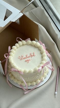 a white cake with pink ribbon and writing on it sitting in front of a box