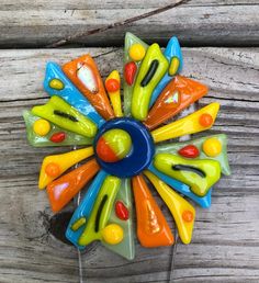 a multicolored glass flower brooch sitting on top of a wooden table next to a piece of wood