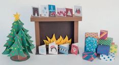 some christmas presents are sitting next to a small tree and fireplace with cards on it