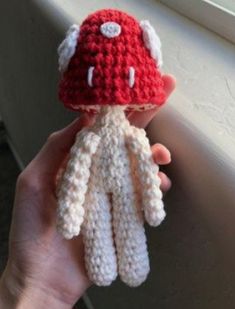 a hand holding a crocheted stuffed animal in front of a window sill