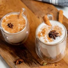 two mugs filled with hot chocolate and cinnamon sitting on a wooden tray next to each other