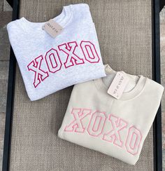 two sweatshirts sitting on top of a chair next to each other, one with an xoxo embroidered on it