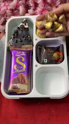 a person is holding a tray with chocolates and other food items in it on a red table cloth