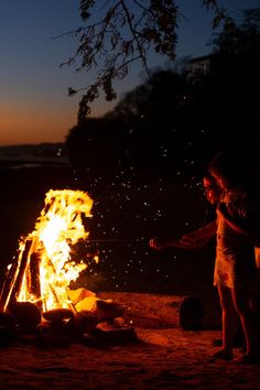 a woman standing next to a fire on top of a field