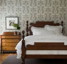 a bed with white sheets and pillows in a bedroom next to a dresser, mirror and lamp