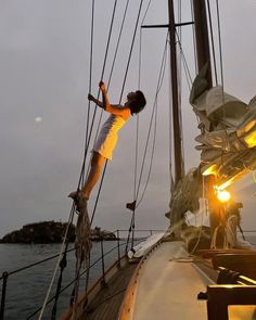 a man standing on the side of a sailboat at sunset with his arms outstretched