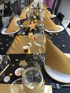 a long table is set with gold and black plates, napkins, and wine glasses