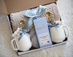 two white coffee mugs in a box with blue ribbon and bows on the handles