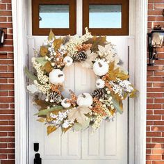 a white door with a wreath on it and pumpkins hanging from the front window