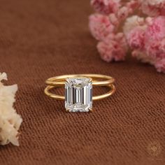 an emerald cut diamond ring sitting on top of a brown surface next to flowers and shells