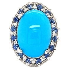 The Natural Oval Cut Turquoise is 6.48 Carats and is surrounded by a cluster of beautifully set diamonds and sapphires. There are 16 Round Cut Diamonds that weigh 0.19 Carats and 16 Round Cut Sapphires that weigh 0.79 Carats. The total carat weight of the ring is 7.46 Carats. Clarity and Color of Diamonds are VS-H. The turquoise measures at 18 mm x 12 mm and the face of the ring measures at 24 mm x 18 mm. The ring is crafted in 14 Karat White Gold and weighs approximately 7.4 grams It is a size Luxury Fine Jewelry Turquoise Ring With Diamond Accents, Blue Cluster Rings With Multi-stone, Blue Cabochon Ring In Fine Jewelry Style, Blue Cabochon Fine Jewelry Ring, Fine Jewelry Blue Cabochon Ring, Blue Turquoise Ring With Diamond Accents For Wedding, Oval Blue Multi-stone Gemstones, Wedding Turquoise Ring With Diamond Accents, Oval Blue Cabochon Gemstones