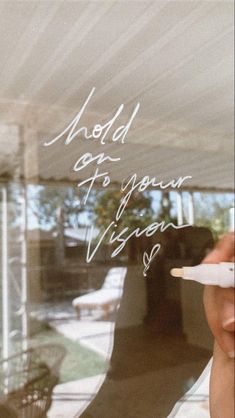 a person holding a pen and writing on a glass window with the words hold up to your vision