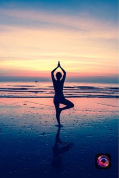 a woman is doing yoga on the beach at sunset with her hands in the air